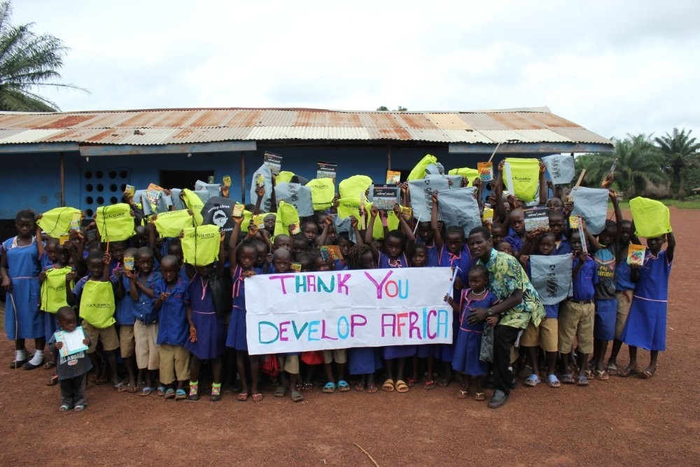 (c) Develop Africa. Pupils with gifts of bags from Develo Africa woth a banner thanking Develop Africa for the provision of school bags.